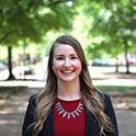 Alexa is pictured from the shoulders up wearing a red shirt and black jacket. She has fair skin, long blonde hair and is smiling. 