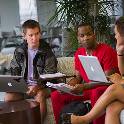 Three students sitting on sofa with their laptops and notes to study