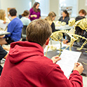 A student in a read hoodie looks toward his professor who is instructing a lab class.