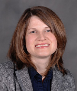 Kristy Welshhans, a White woman with should length brown hair smiles at the camera for a professional headshot.