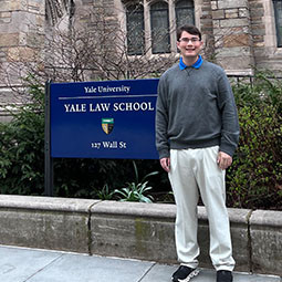 Graduate standing and smiling in front of a Yale Law School sign.