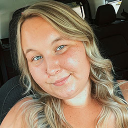 Portrait of a graduate with long blonde hair smiling inside a car.