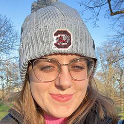 Graduate wearing a USC beanie and glasses, smiling in a park on a sunny day.