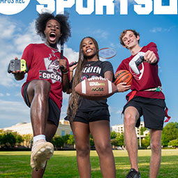 Three students in sports gear posing energetically in front of a “Campus Rec Sports” banner.