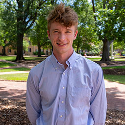 Graduate in a button-down shirt smiling on the University of South Carolina campus.