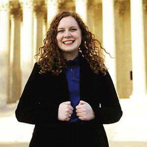 Student in a formal outfit smiling confidently in front of the columns of the U.S. Supreme Court.