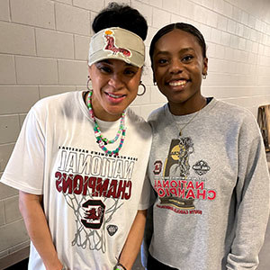 Two women wearing USC National Champions gear, smiling and standing side-by-side indoors.