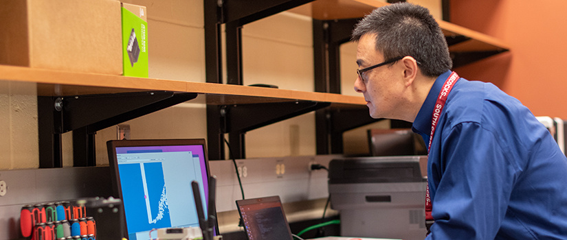 Yi Wang stands in his research lab working on a computer.