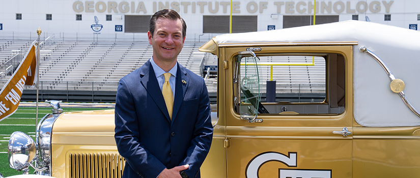 Ryan Alpert stands beside Georgia Tech’s gold and white Ramblin’ Wreck car on the football field at Bobby Dodd Stadium.