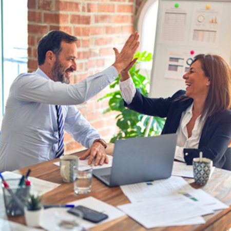 Two people smile and give a high five while sitting at a table.