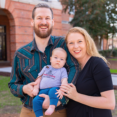 Gannett and Caroline Loftus pose with their baby outside of the school of medicine