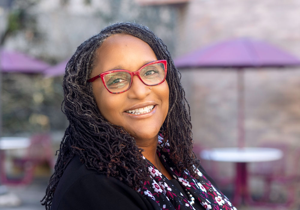 Dr. Gayenell Magwood wears a floral garnet and black scarf and red glasses frames.