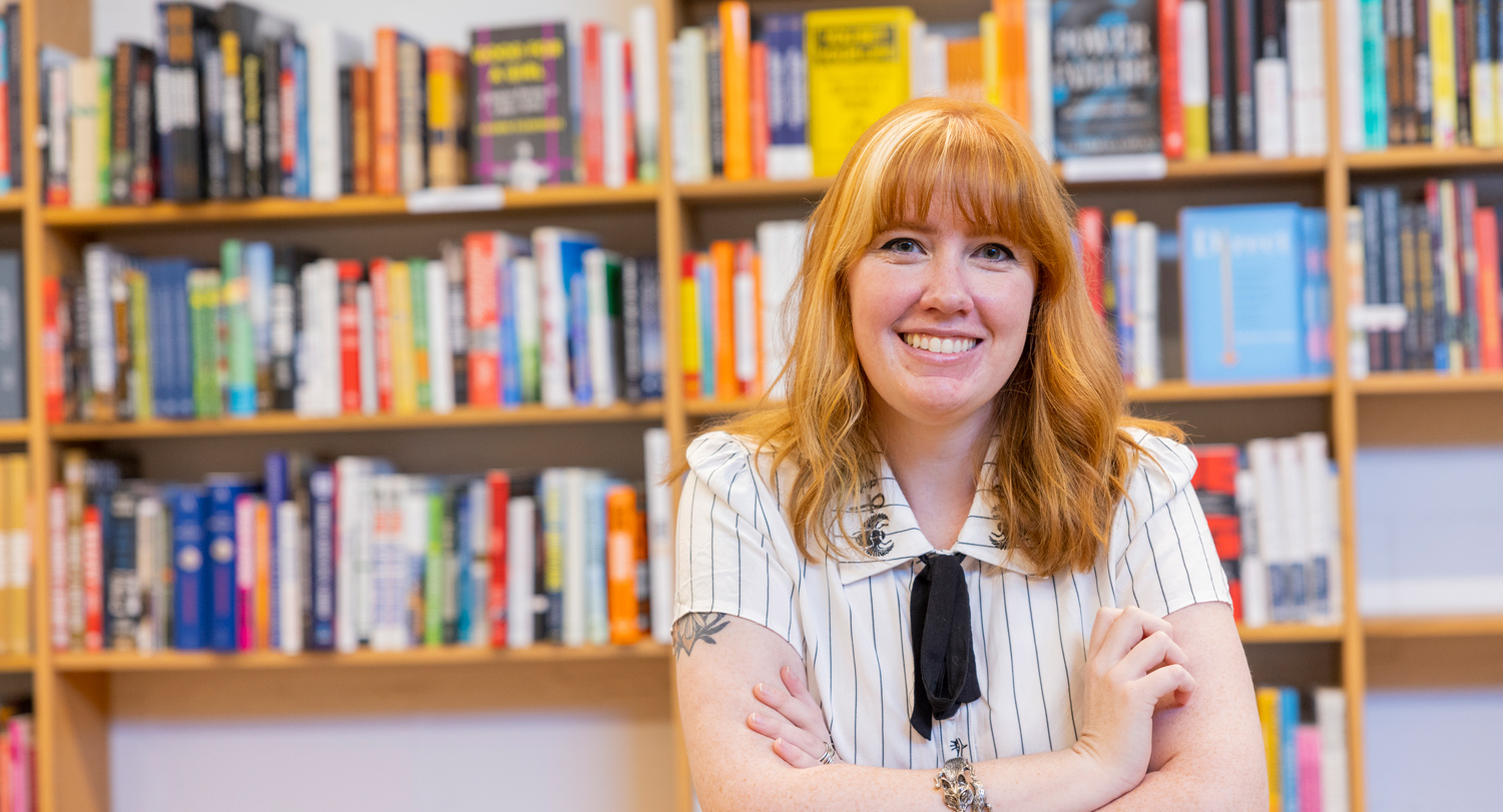 Ashley Poston sits at a table in front of bookshelf