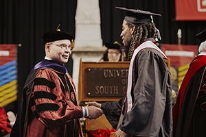 graduating student in cap and gown shakes an official's hand on stage