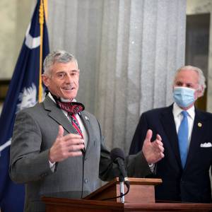 uofsc president bob caslen speaks at a podium while south carolina gov. henry mcmaster looks on