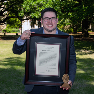 Robert Pokora stands on the horseshoe holding a large framed award