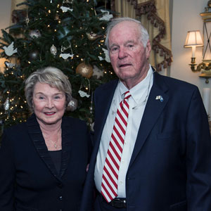 a man and woman stand in front of a christmas tree