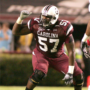 man in garnet football jersey crouches over football and points