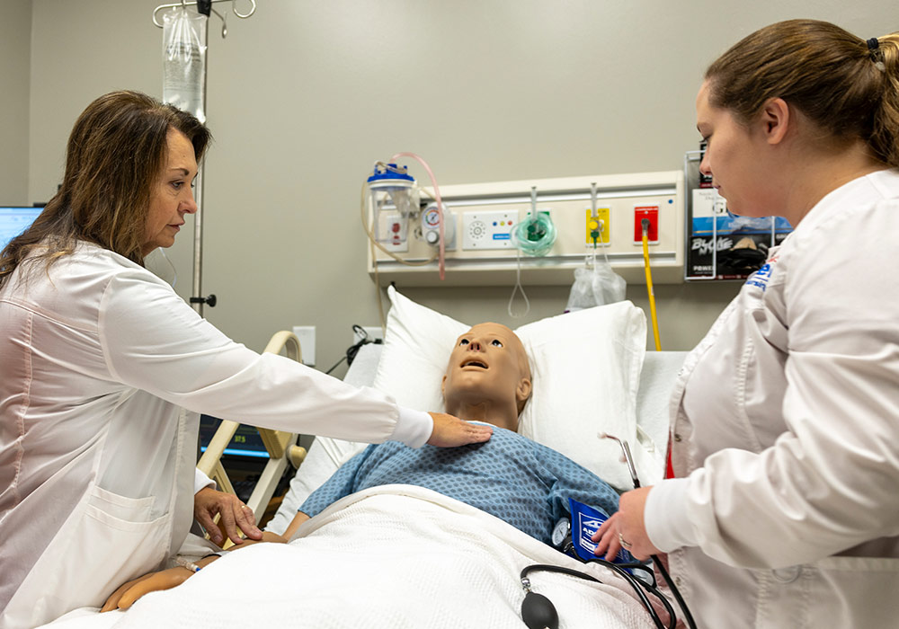 Nursing student leaning over a mannequin listening with a stethoscope. 