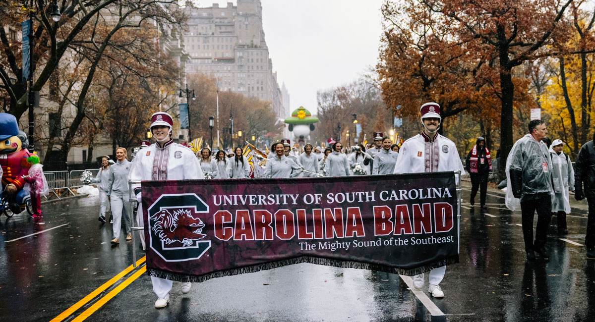 marching band walks in the rain carrying a banner that reads university of south carolina carolina band the mighty sound of the southeast